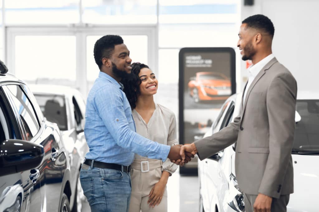 Car Dealer Handshaking With Happy Auto Buyers After Successful Deal In Dealership Store.